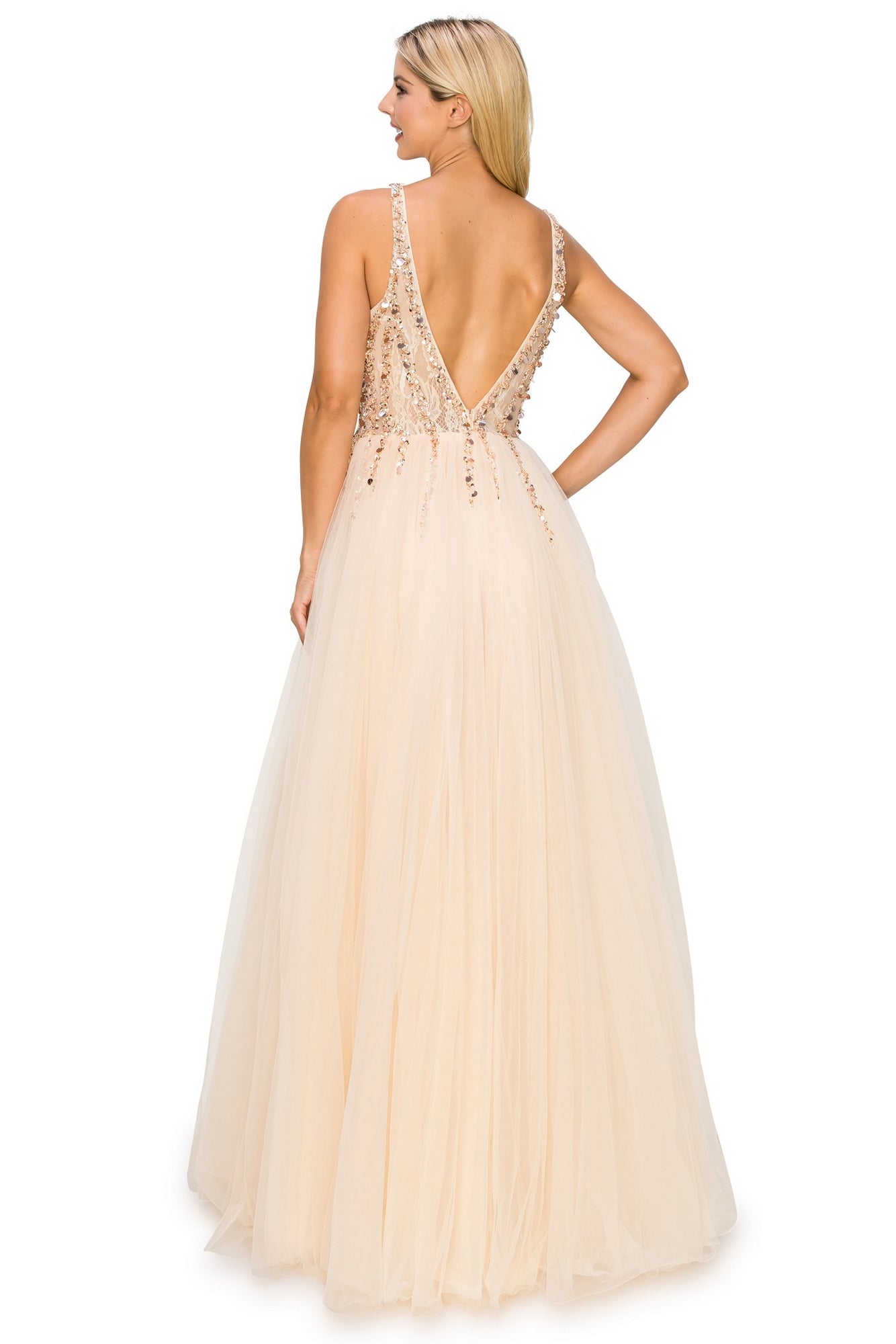 A woman in the Long Tulle Prom Ball Gown with Sequins 8034J—a sleeveless, floor-length blush dress with a sequined v-neck bodice and deep V-back—stands facing away, an elegant plus size prom choice.